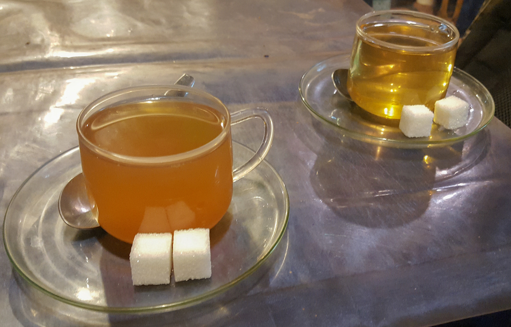 Two cups of tea in clear coffee cup with two cubes of sugar on each clear saucer